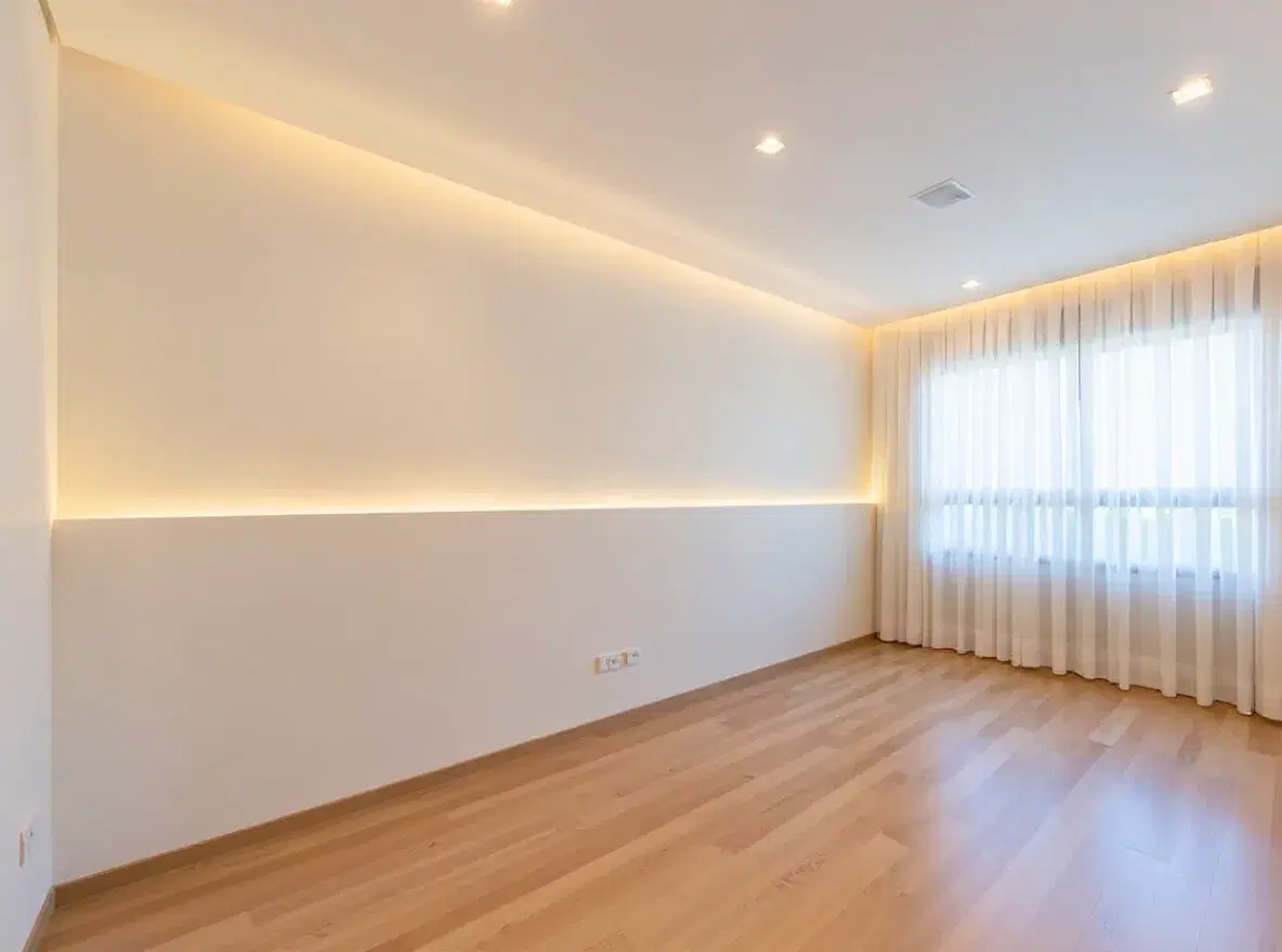 Quarto vazio com piso de madeira, cortina na janela e uma faixa de luz na parede, na foto original